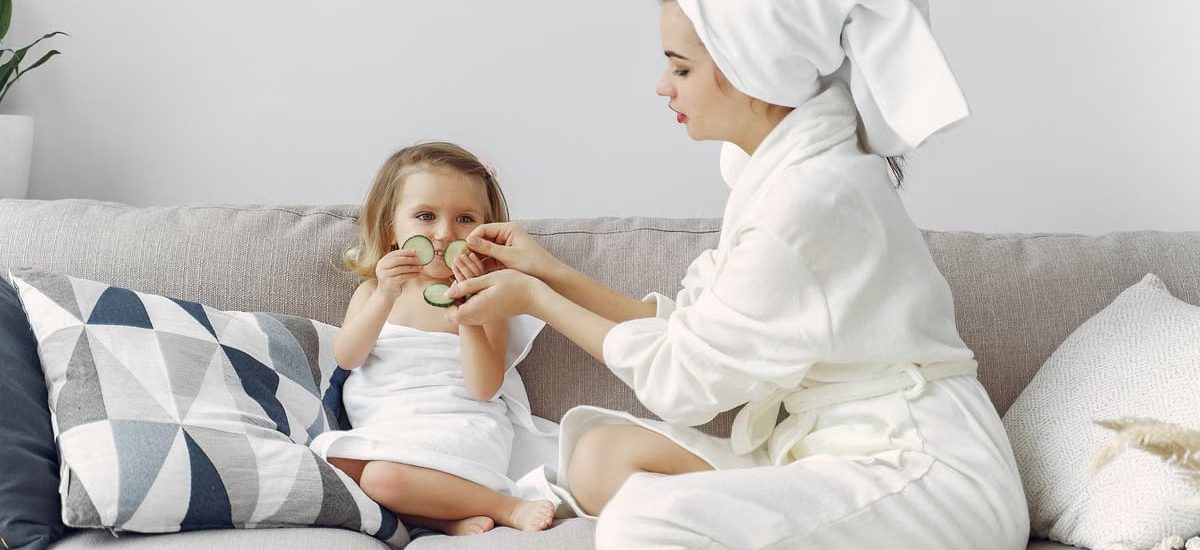 A mother and daughter enjoy a spa day at home, bonding on the couch with cucumber slices.